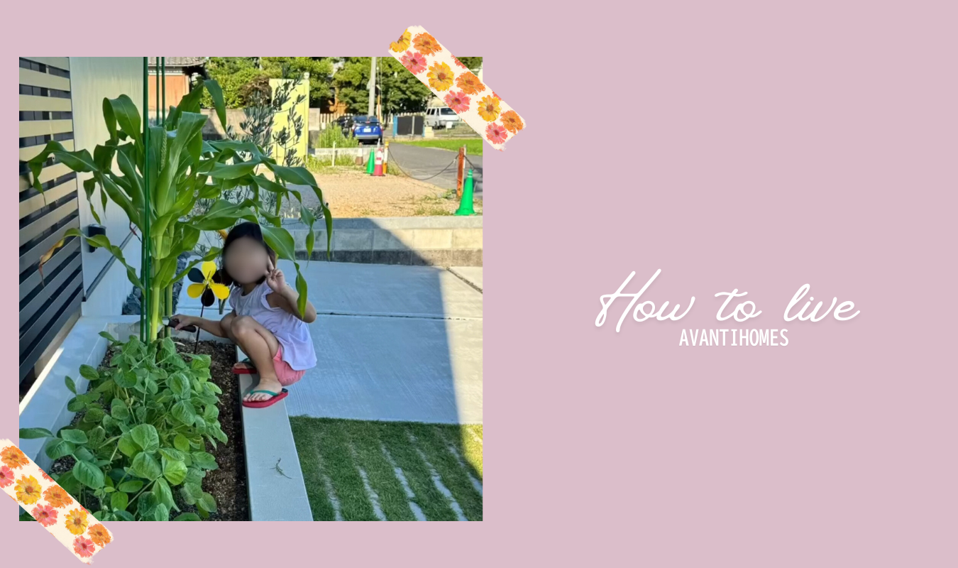 玄関横の家庭菜園で育つ野菜のそばにしゃがみ、庭の自然に触れる女の子の様子